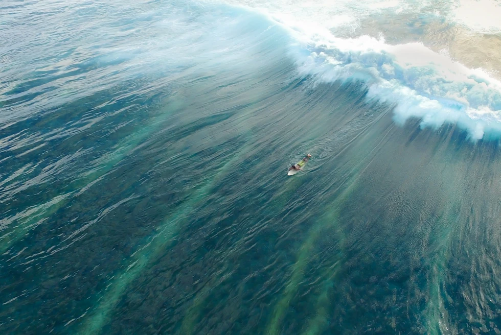 A surfer on a white surfboard in the Maldives with blue water and white water waves crashing.