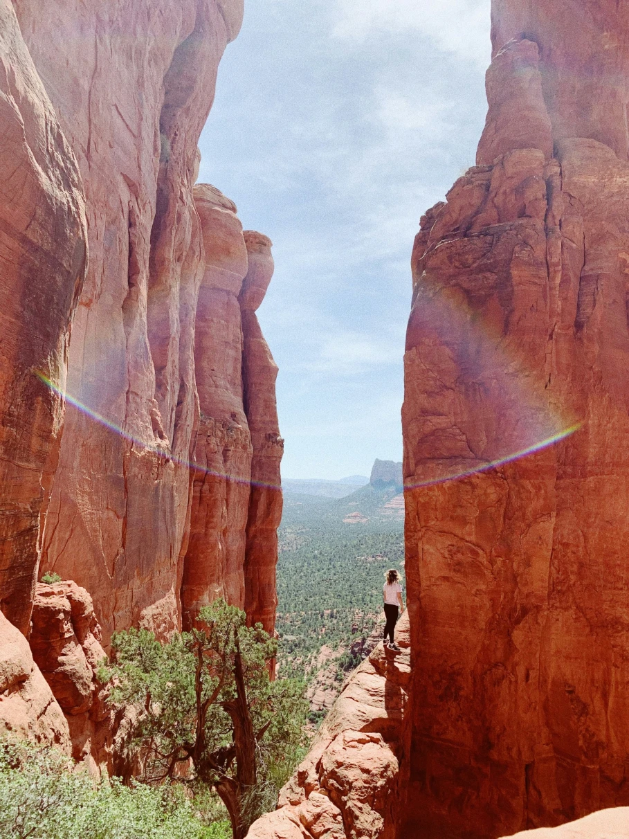A picture of a person climbing a cliff during daytime with a small rainbow in the distance.