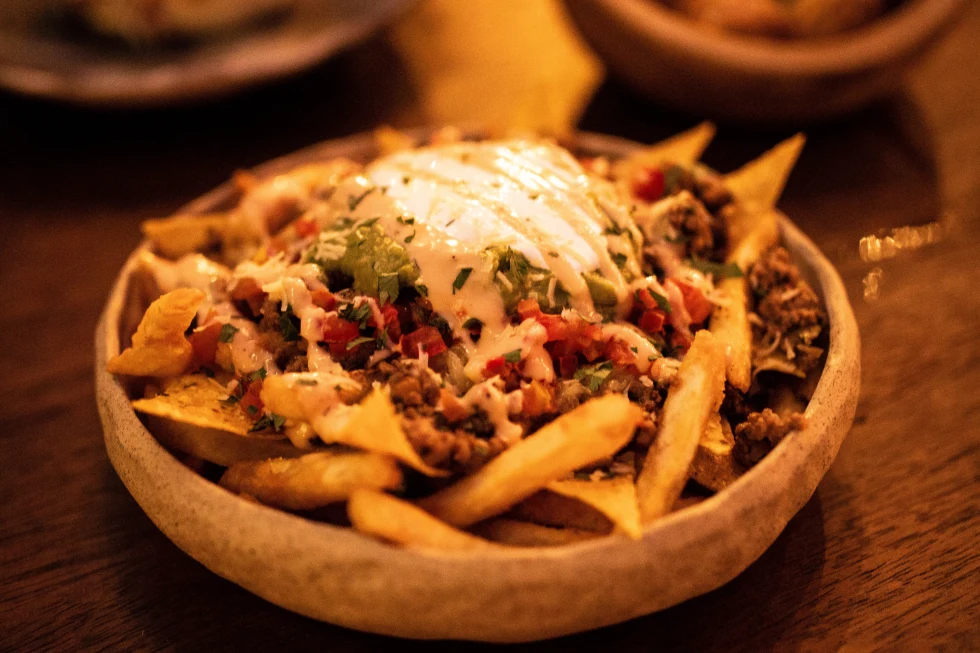 Bowl of fries with toppings on wooden table
