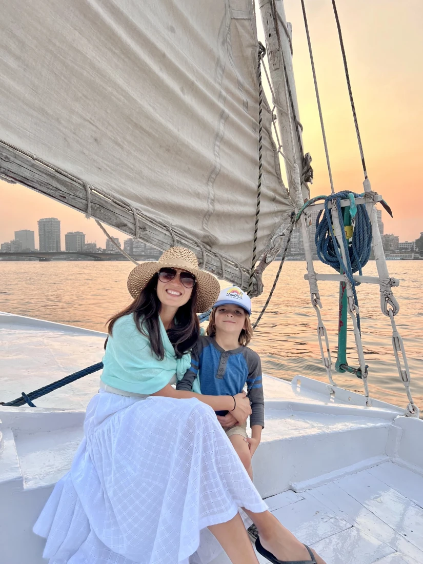 a woman in a sunhat and sunglasses sits on a sailboat with her young daughter