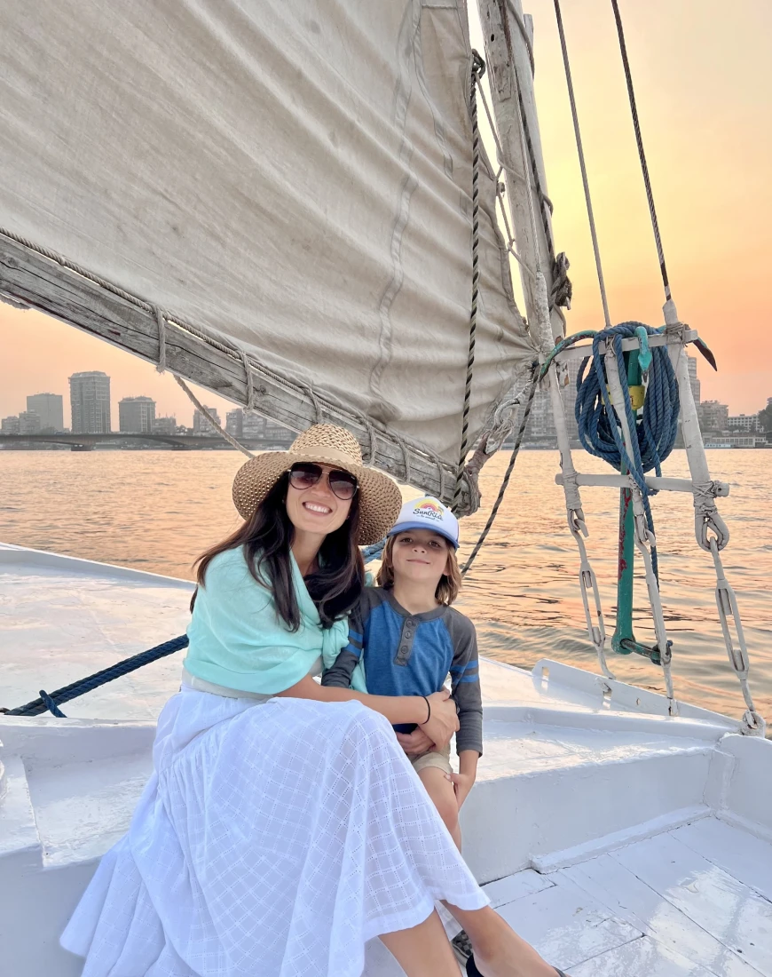 a woman in a sunhat and sunglasses sits on a sailboat with her young daughter