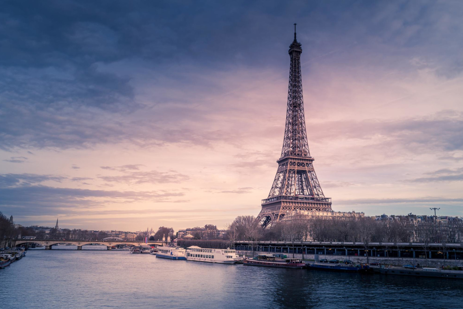 The Eiffel Tower on a dark cloudy day next to La Seine in Paris.