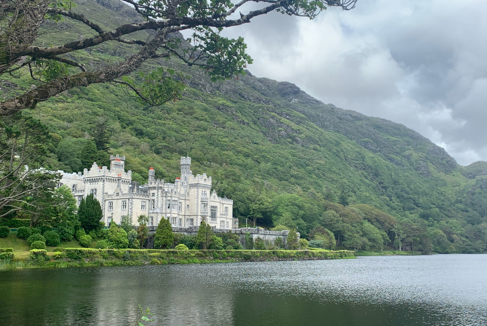 Large white building next to body of water and trees with cloudy skies during daytime