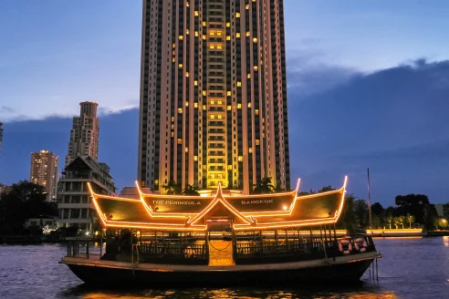 an illuminated boat on a river in front of a high tower