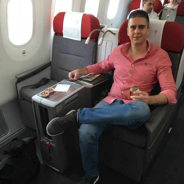 Fora travel agent Boris BK wearing red shirt and jeans sits in airplane seat