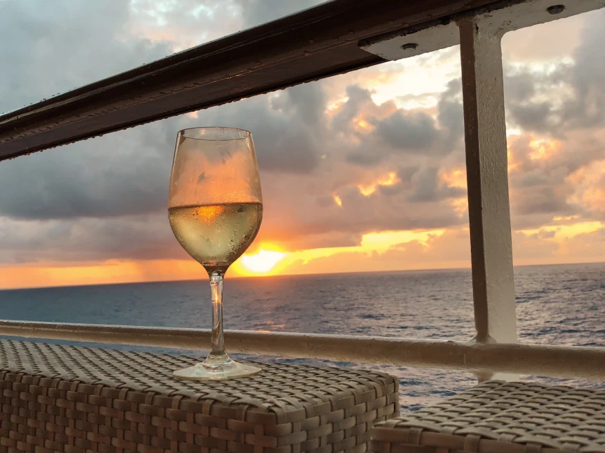 Glass of wine on chair with sunset in the background over body of water