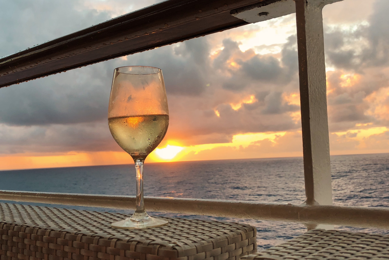Glass of wine on chair with sunset in the background over body of water
