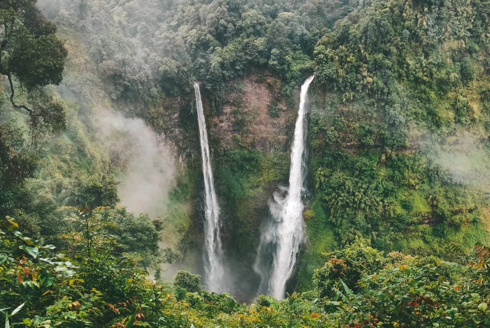 Two beautiful waterfalls coming out of a green mountain.