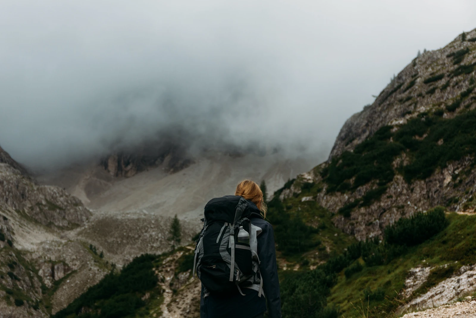 Person wearing backpack and orange hat faces mountains in the background covered in fog in Italy