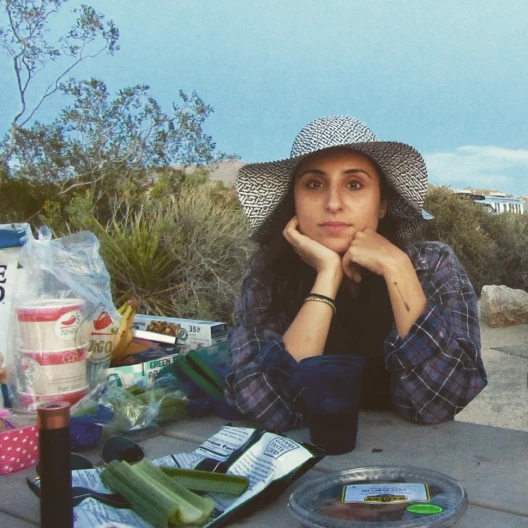 Travel advisor Michelle Oliveira wears a sun hat and plaid shirt at a picnic table in the desert
