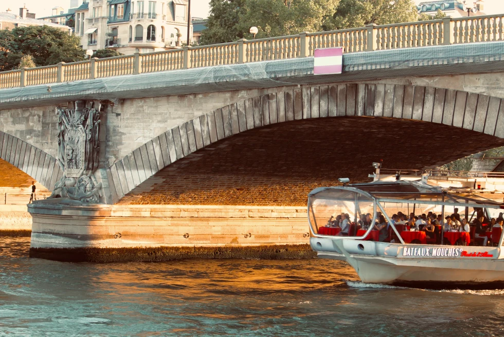 A boat passing below the bridge in a river in Paris