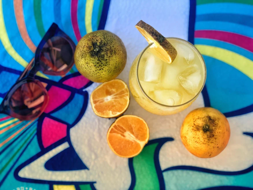 a fruity cocktail with sliced orange and sunglasses lay beside it on a colorful table