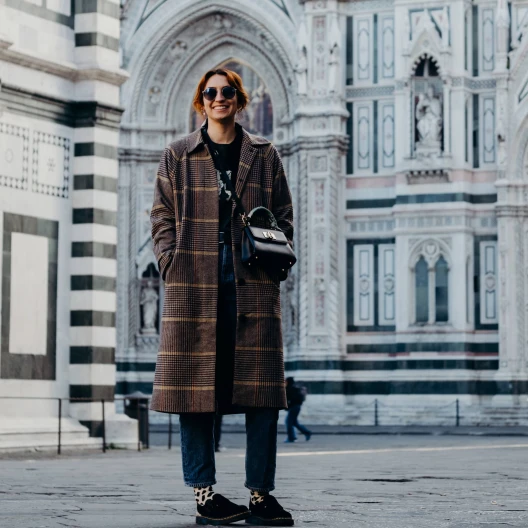 Travel Advisor Sydney Vaccaro in a long coat, sunglasses and a cross body bag. 