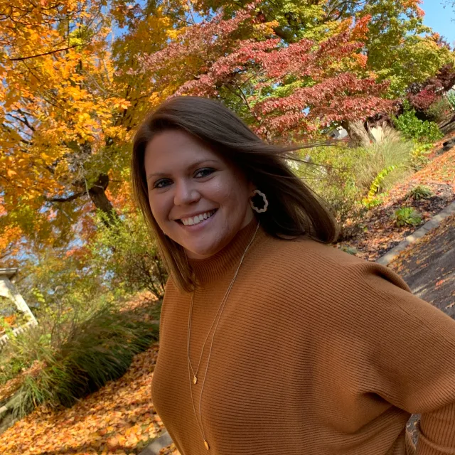 Travel Advisor Alexa Campbell with an orange sweater and fall leaves in the back.