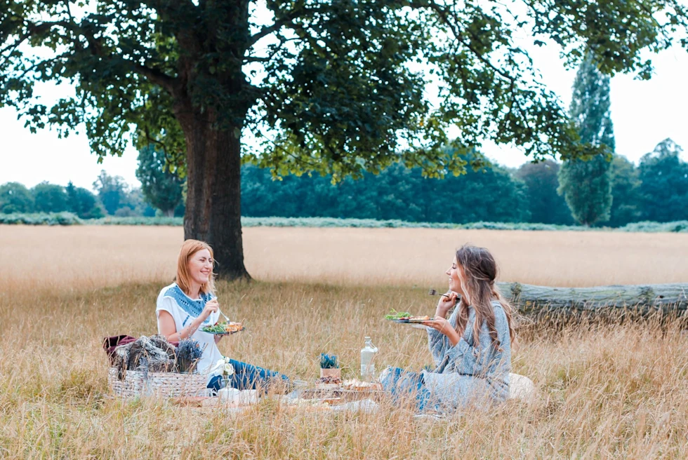 Two girls sitting in countryside and having picnic.