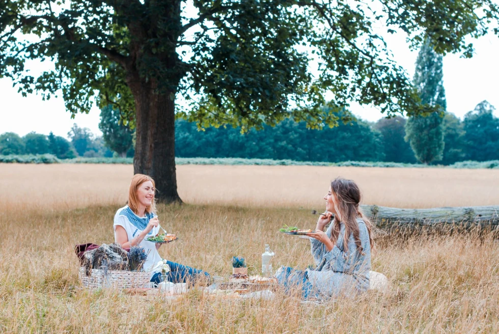 Two girls sitting in countryside and having picnic. 