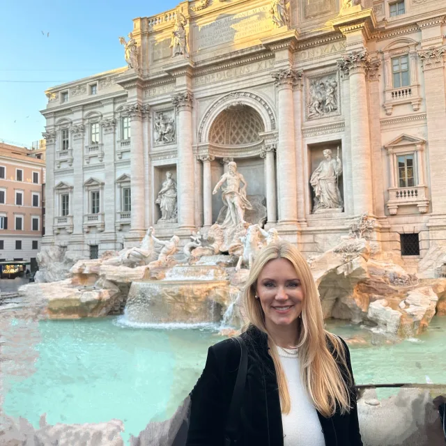 Travel Advisor Yennifer Arguelles stands in front of the Trevi Fountain in Rome wearing a white shirt and black coat