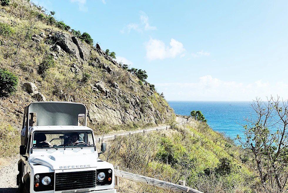 car on unpaved road next to body of water during daytime