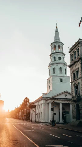 A tall, white church in a city street during a sunrise