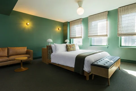 A large green bedroom with a leather couch and a wooden bed in the center of the room.