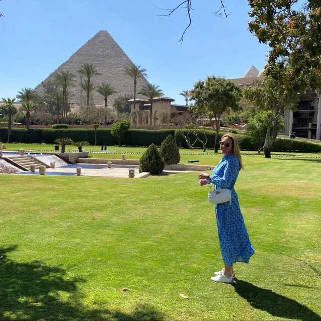 Picture of Tamara wearing a blue dress and standing on green grass at the Marriott Mena House in Cairo, Egypt overlooking one of the Great Pyramids of Giza 