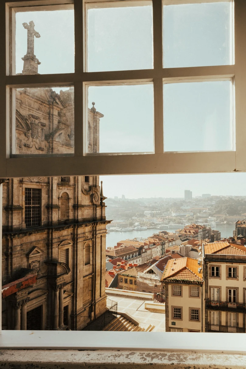 The image offers a view of a historic cityscape through a large window, contrasting the interior with the external architecture.