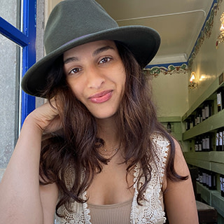 A woman, Rhea Karimpanal, is wearing a hat and smiling