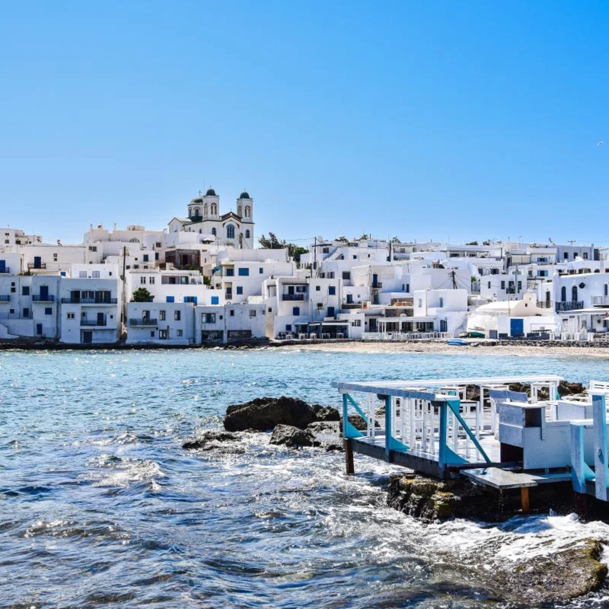 White and blue buildings in front of ocean on clear day in Greece.