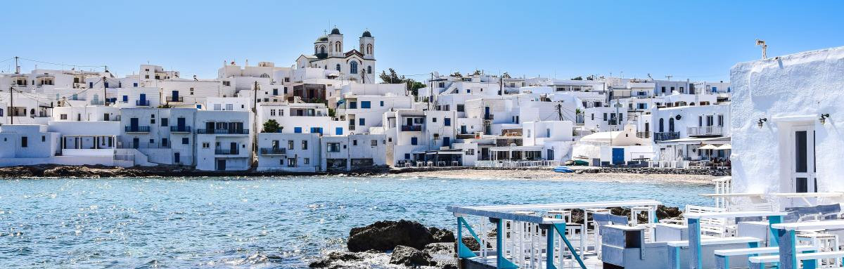 White and blue buildings in front of ocean on clear day in Greece.