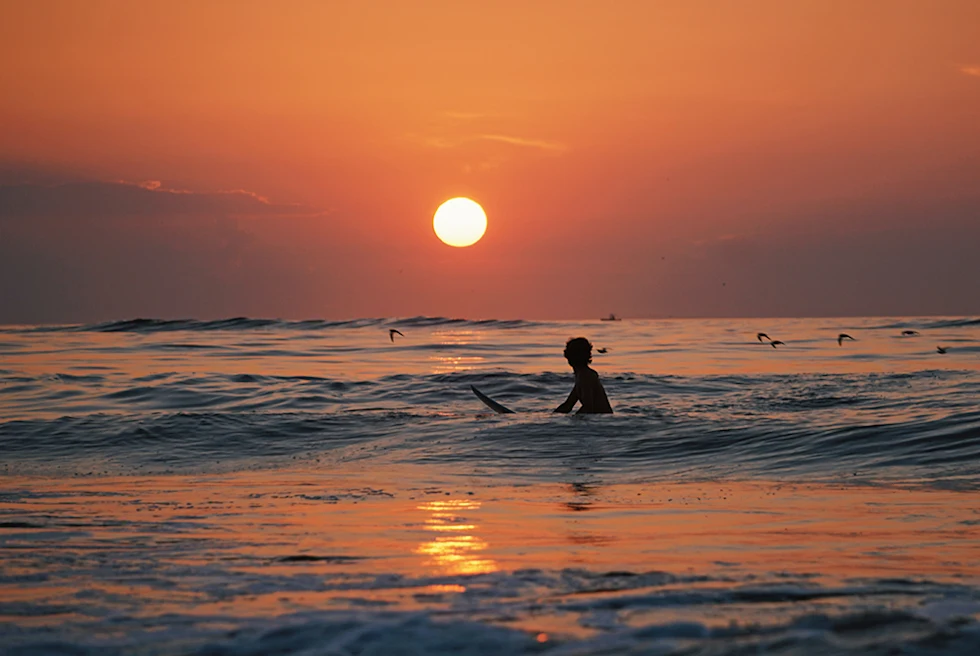 surfing at sunset in las catalinas costa rica with birds flying by and light reflecting on ocean water