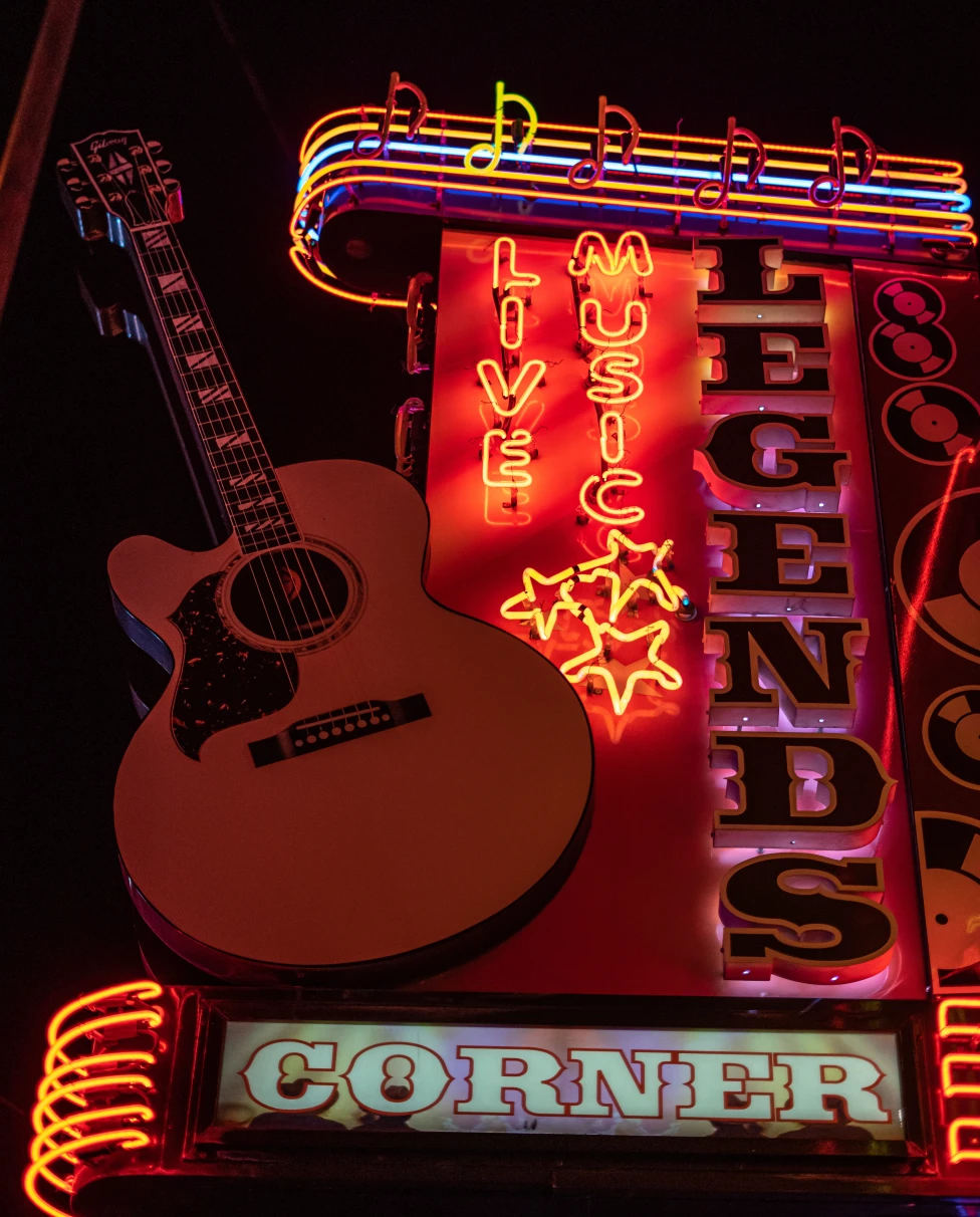 A wall with colorful lights and a writing saying LEGENDS CORNER and guitar hanging on it.