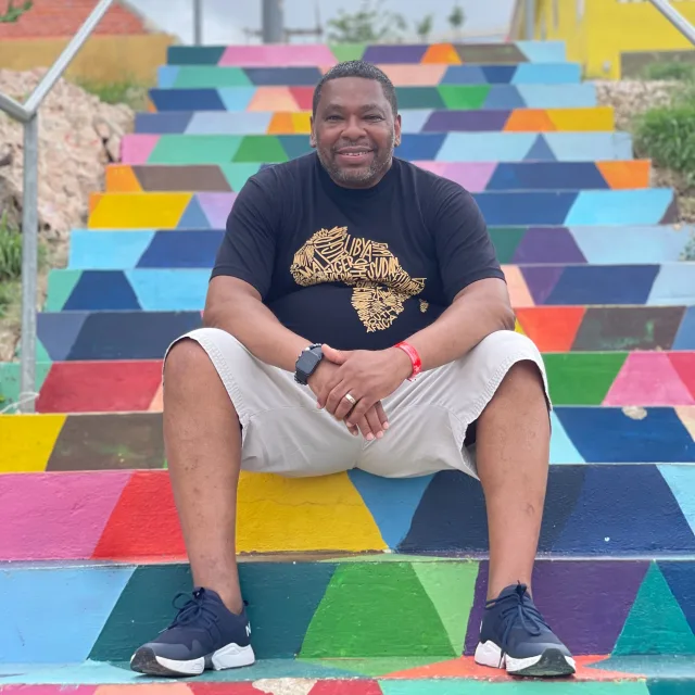 Travel Advisor Jerome Hurt sitting on colorful stairs wearing a black t-shirt and white shorts.