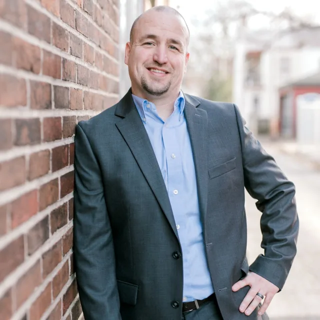 Joshua Bogner in a suit posing against a brick wall.