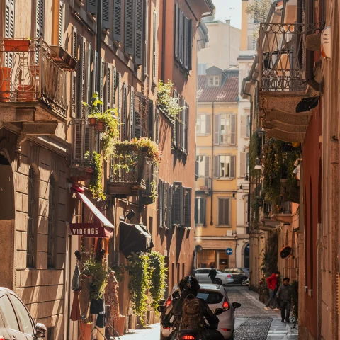 A cobblestone street in Milan with a scooter and some cars. 