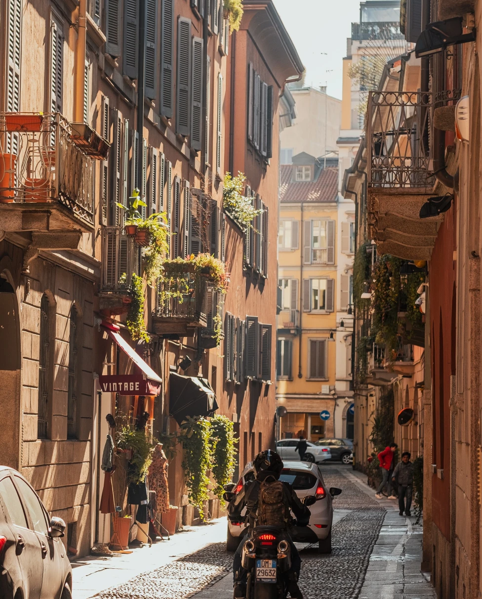 A cobblestone street in Milan with a scooter and some cars. 