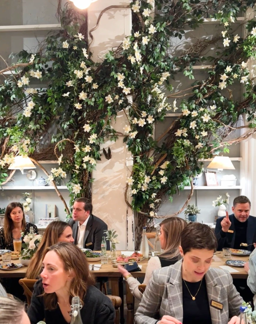 people sit at a wooden table and eat in front of a wall covered with decorative vines
