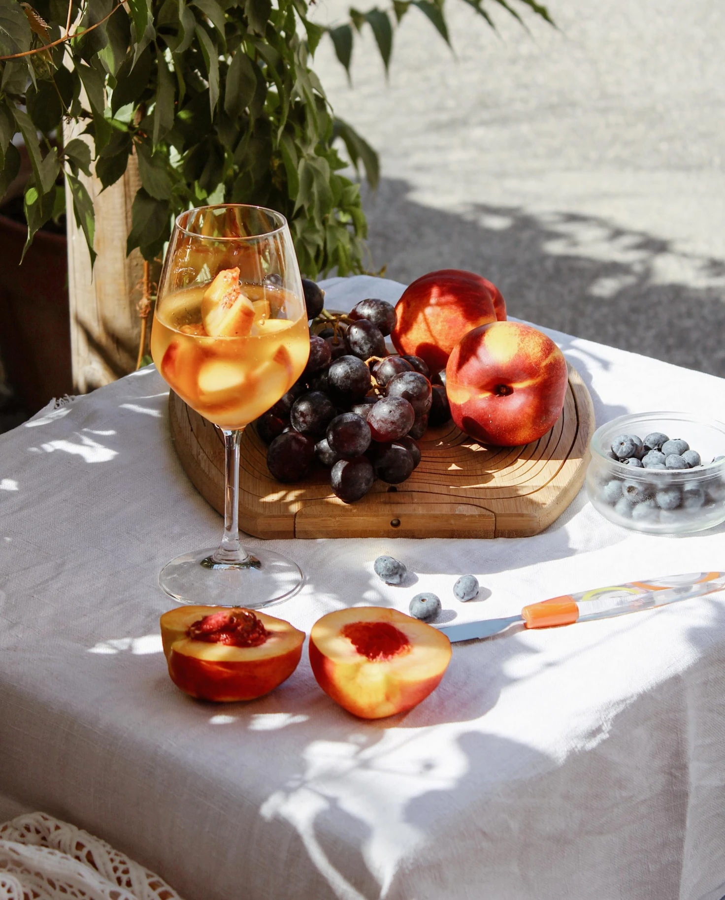 a glass of white wine with a plate of grapes and peaches resting on a white tablecloth