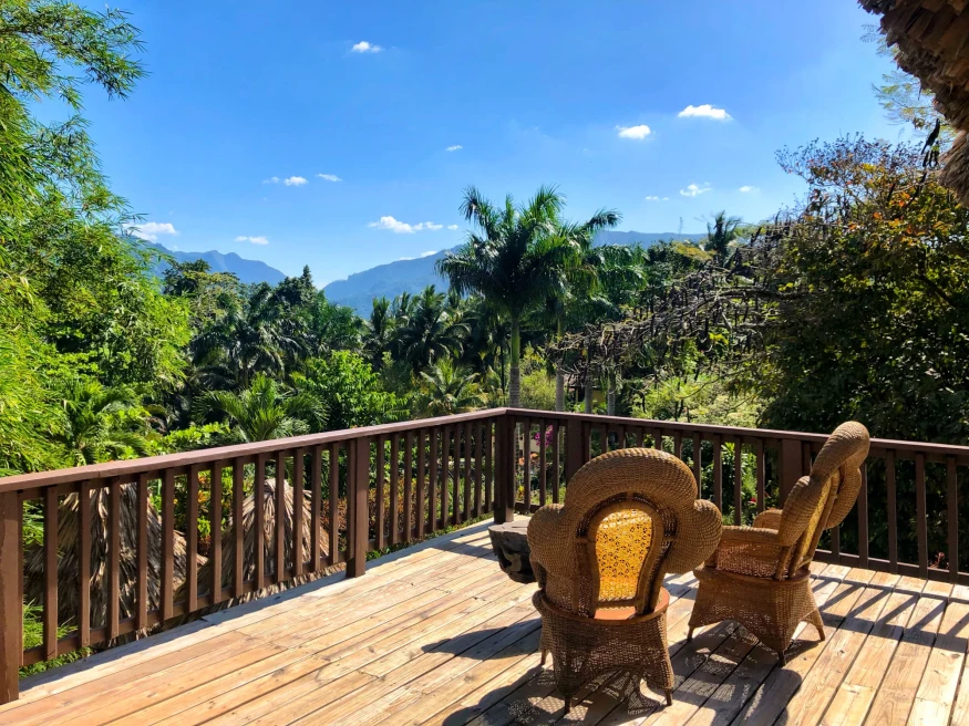 two wicker chairs on a balcony overlooking the jungle on a sunny day