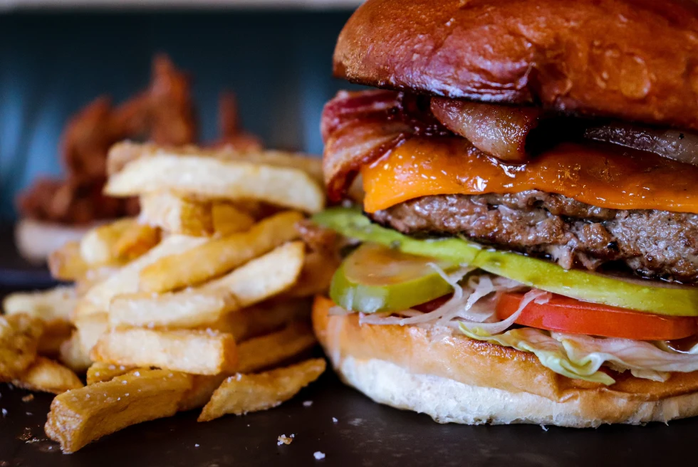 Cheeseburger with pickle and tomato on a black plate with french fries