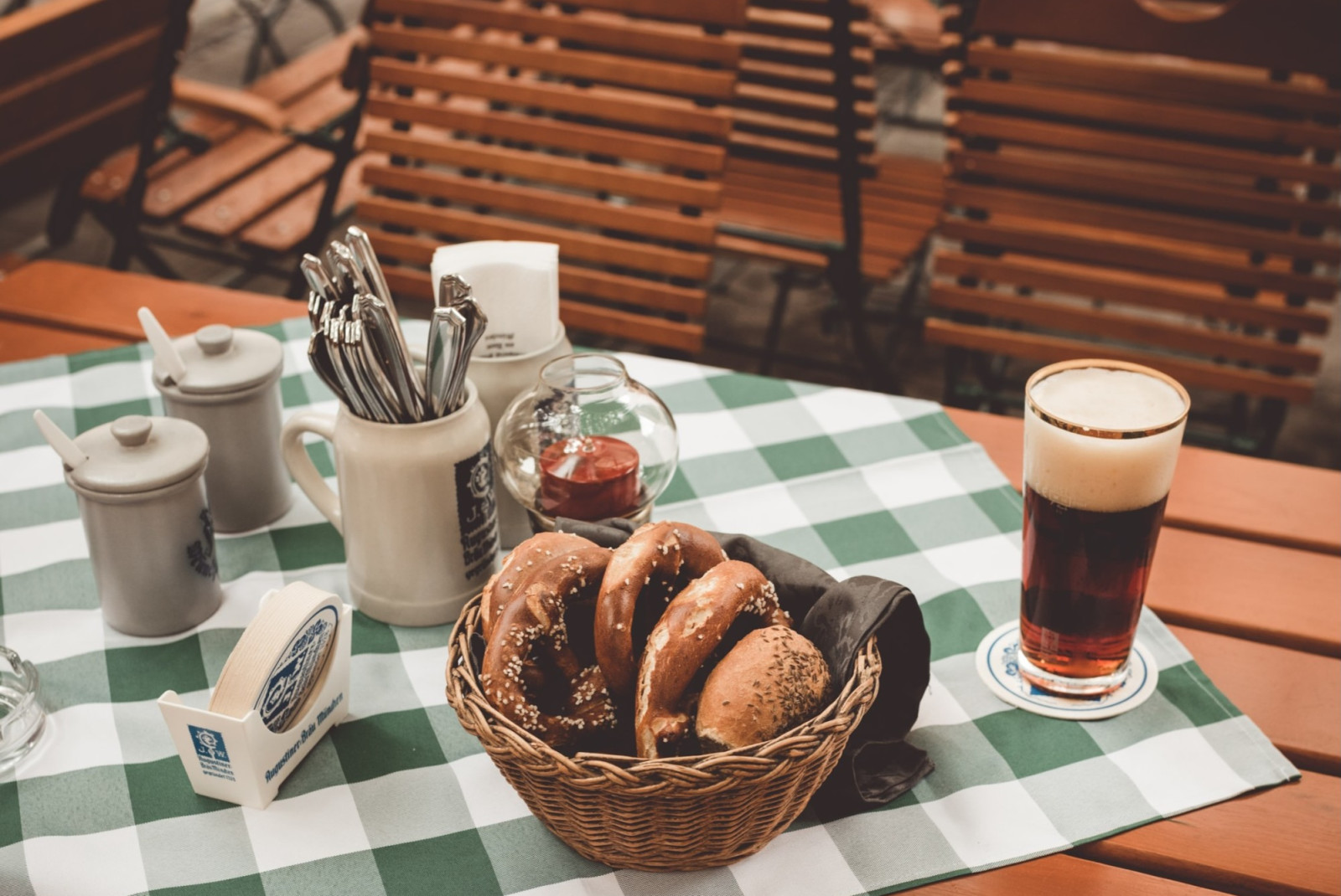 Pastries in basket with beer and silverware on plaid table cloth on picnic table.