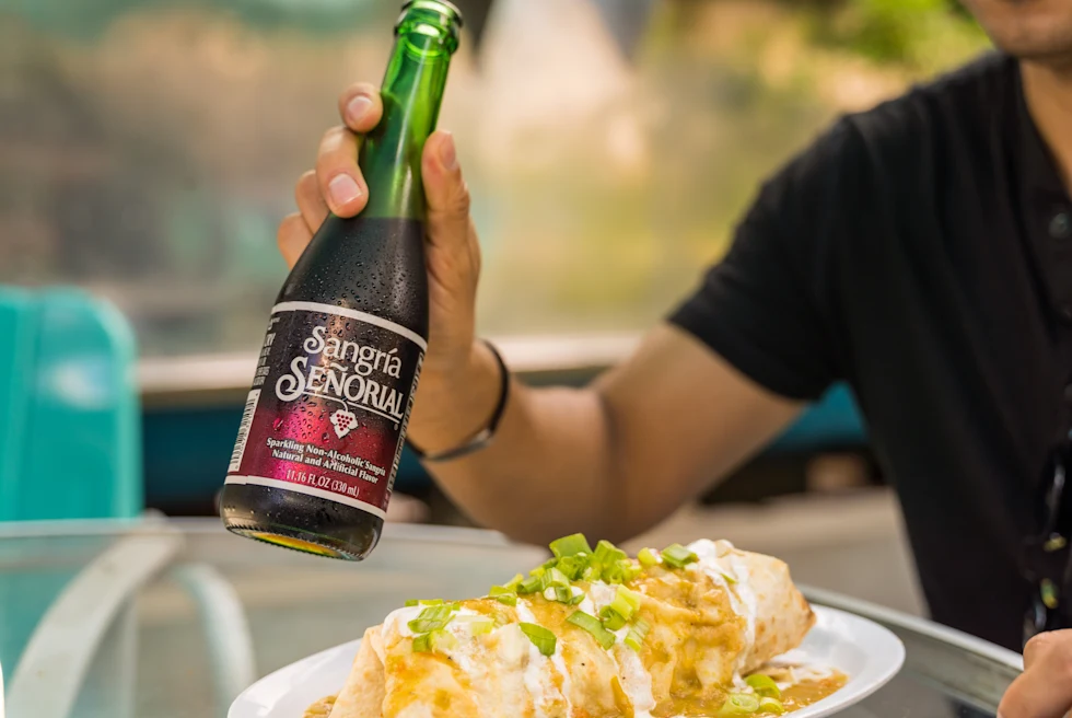 A boy holding wine bottle in hand and having food.