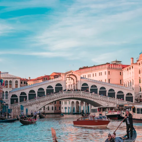 An aesthetic view of a riven passing through the city with a boat in it near the bridge, in Italy.