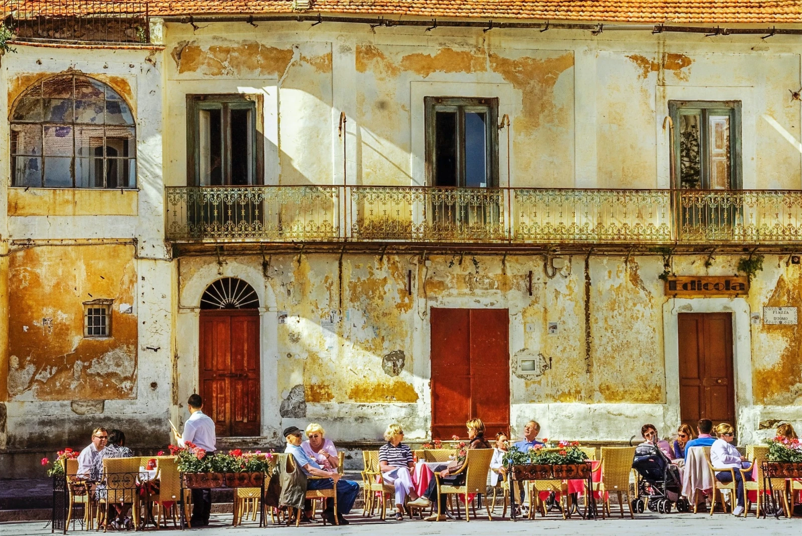 people sitting and chatting at a café in front of an old façade