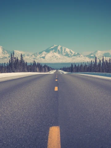 Empty highway stretch in Alaska towards snowy mountains. 