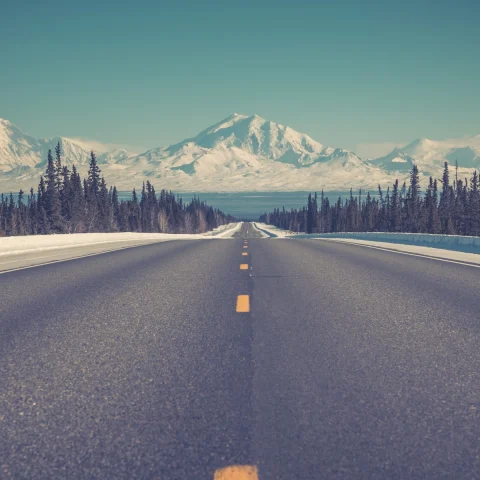 Empty highway stretch in Alaska towards snowy mountains. 