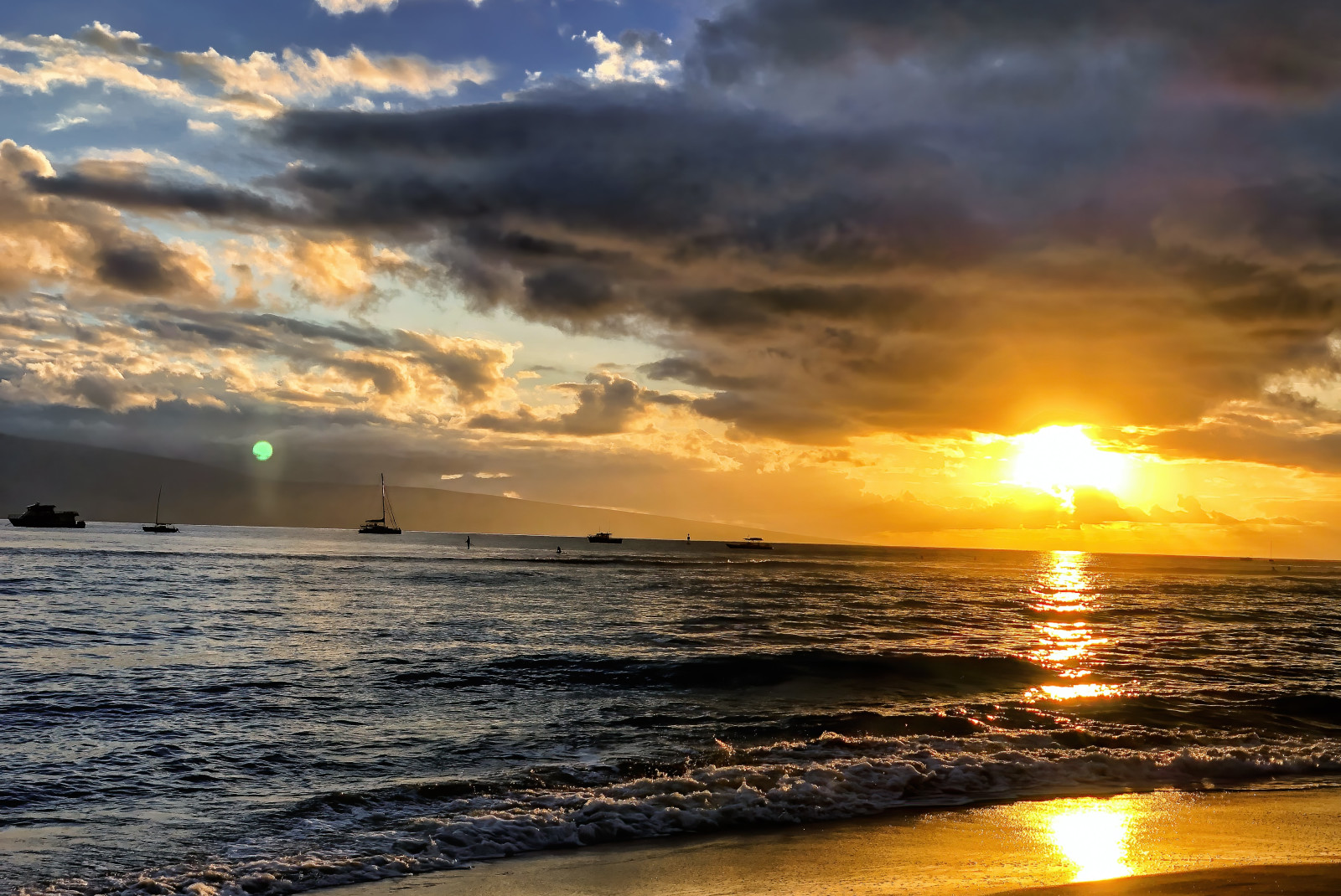 A yellow sunset over the water with four boats floating in Maui, Hawaii.