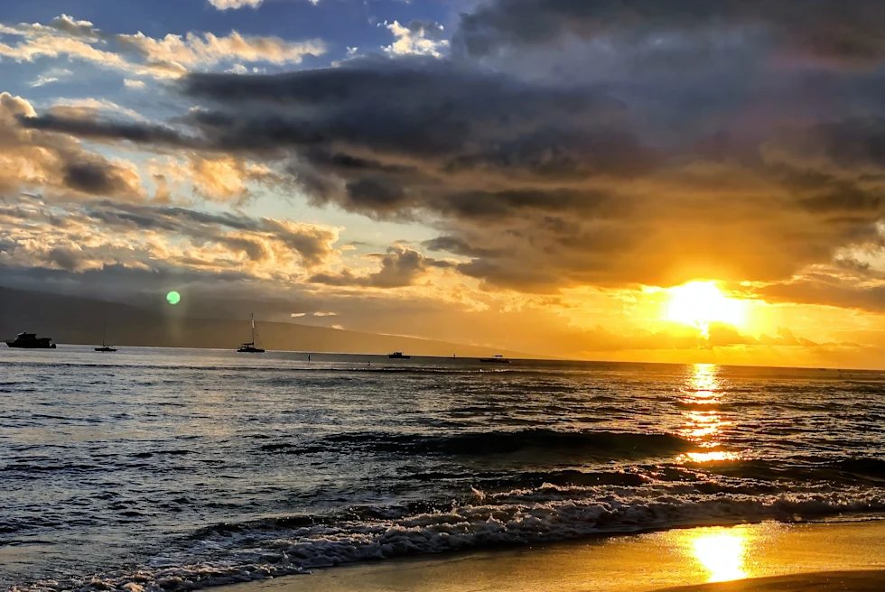 A yellow sunset over the water with four boats floating in Maui, Hawaii.