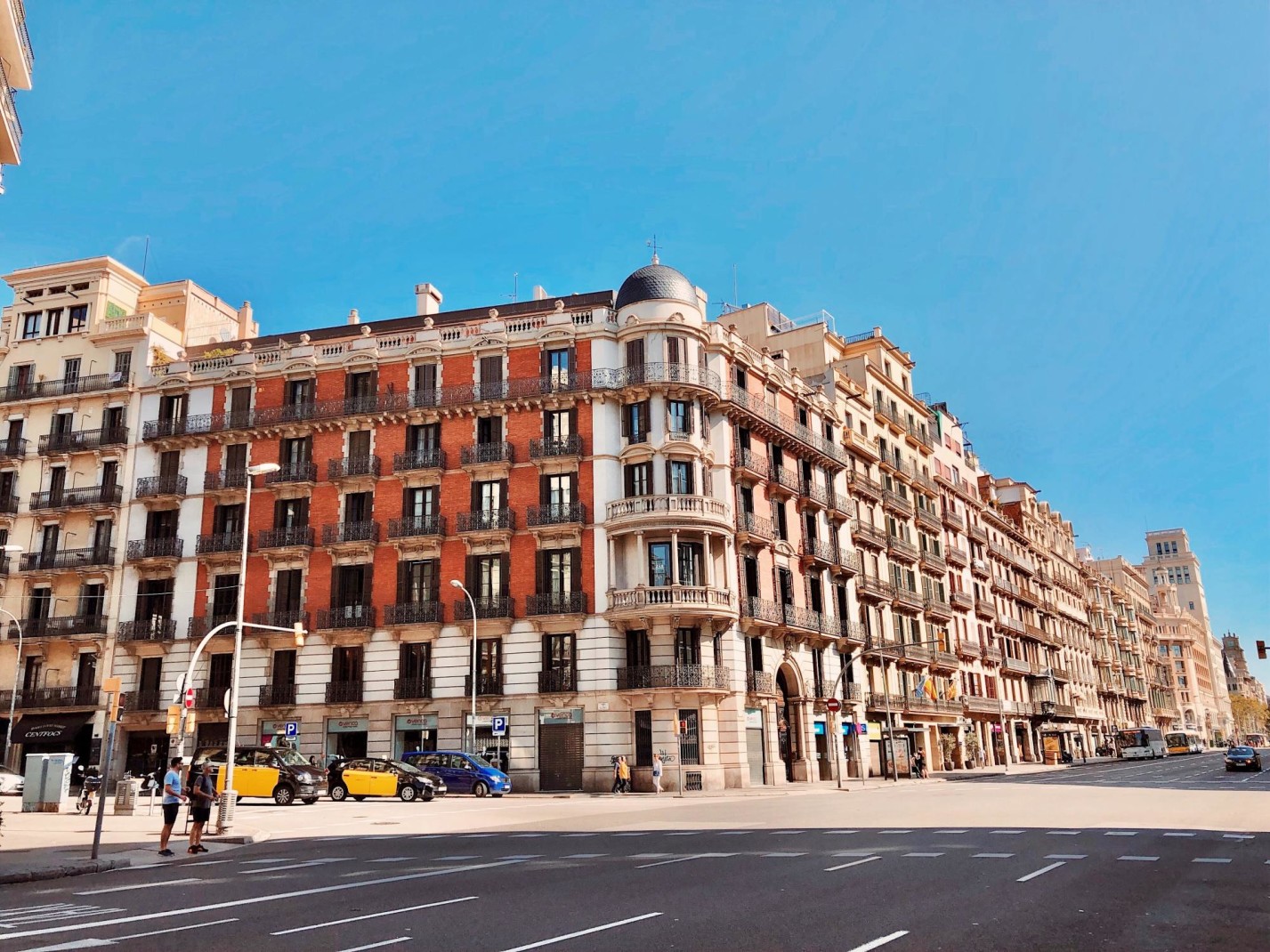Historical buildings on street with few people and cars in Barcelona on clear day.