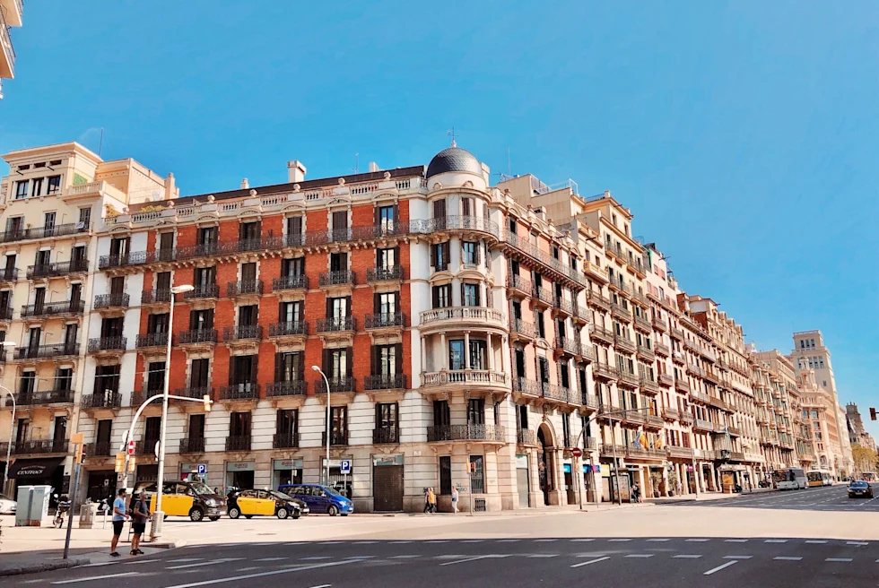 Historical buildings on street with few people and cars in Barcelona on clear day.