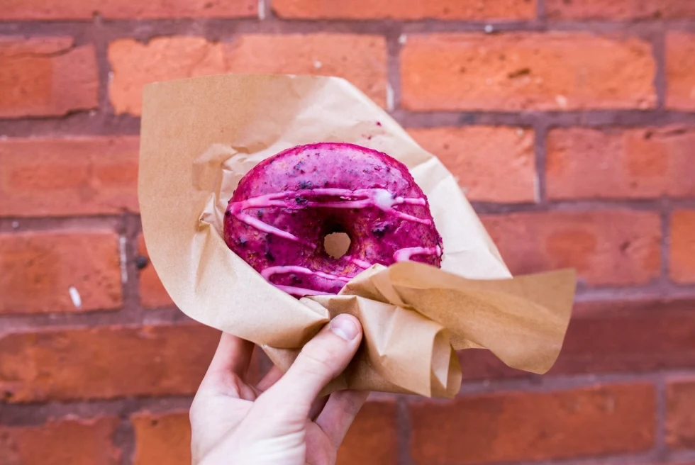 hand holding a purple donut in brown paper